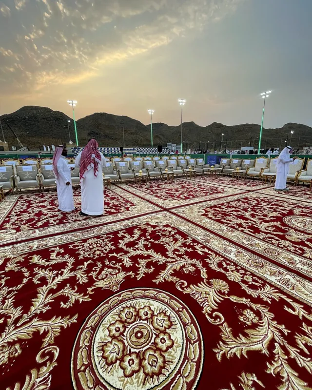 ميدالية السجاد الأحمر الملكي في وسط ساحة احتفال اليوم الوطني بخليص، وخلفها صفوف الجلسات والجبال