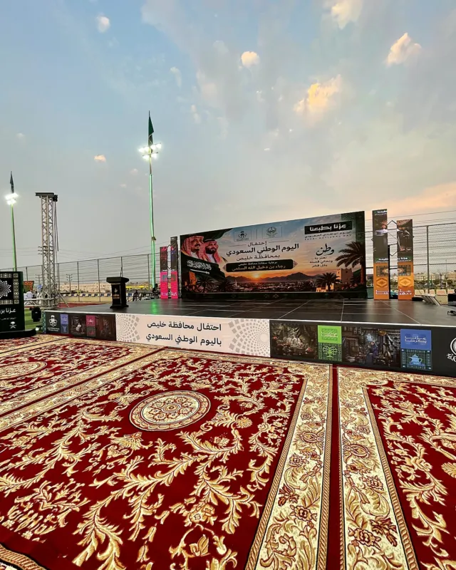 مسرح احتفال محافظة خليص باليوم الوطني السعودي بشاشة كبيرة، وأمامه ساحة مفروشة بسجاد أحمر ملكي بنقوش ذهبية